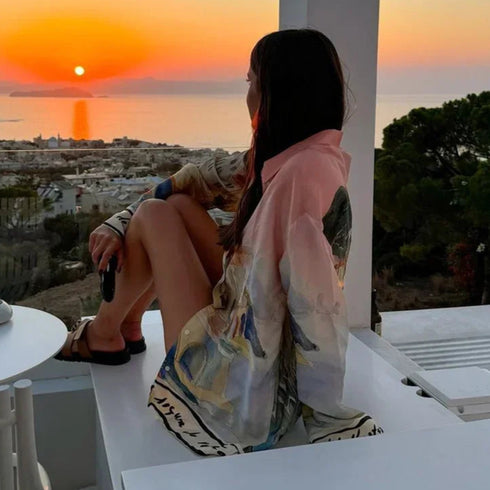 Woman sitting on a balcony overlooking a sunset over a cityscape